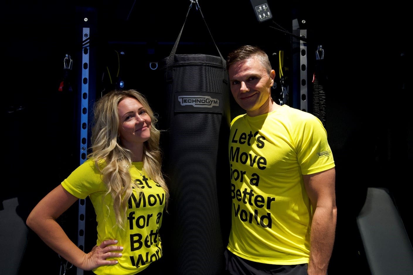 A man and woman posing in front of a punching bag.