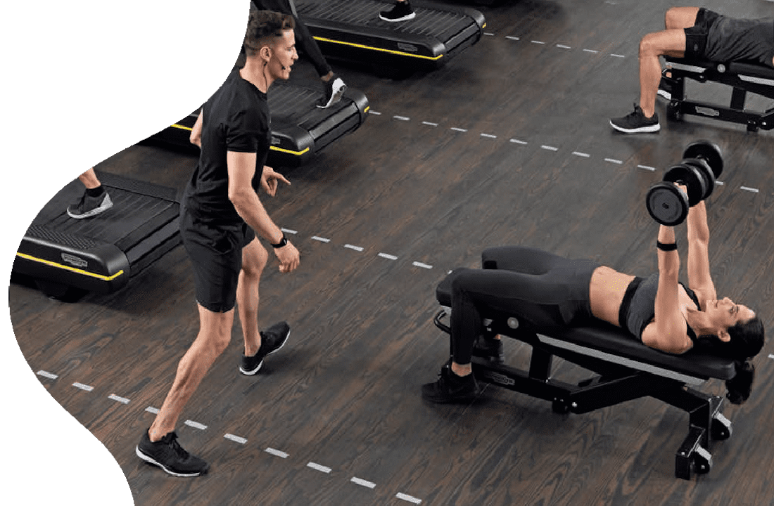 A man is running in the gym while another person sits on a bench.