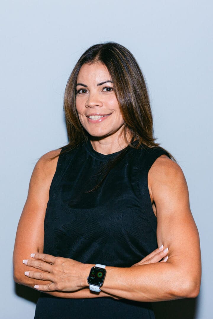 Woman smiling with arms crossed, wearing a black tank top.